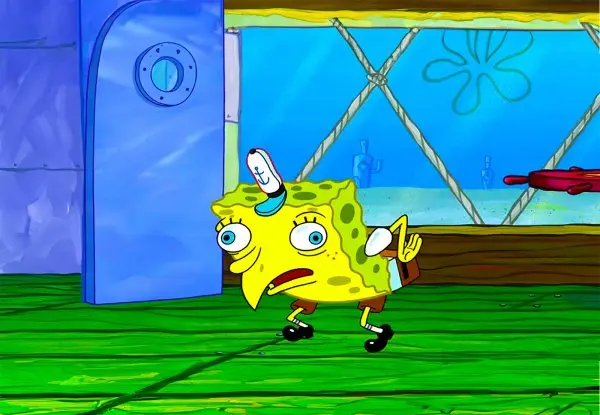 Cartoon sponge hunched in a chicken pose with bulging eyes and bent arms, standing on green grass outside a blue door