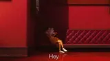 Orange-tracksuited cartoon man in glasses slouched against a red wall and sofa, subtitled "Hey."