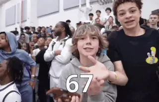 Students in a school gym crowd doing the two-handed '6-7' see-saw gesture, captioned 67