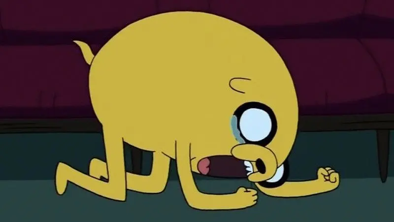 Adventure Time still of the yellow dog Jake on all fours, mouth wide open screaming with a tear, purple couch behind