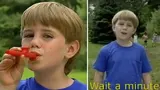 Two stills of a blond boy in a blue T-shirt playing a red kazoo and speaking outdoors, subtitled "Wait a minute"