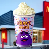 Purple McDonald's cup labeled "Grimace Shake" topped with whipped cream and printed with a smiling purple character