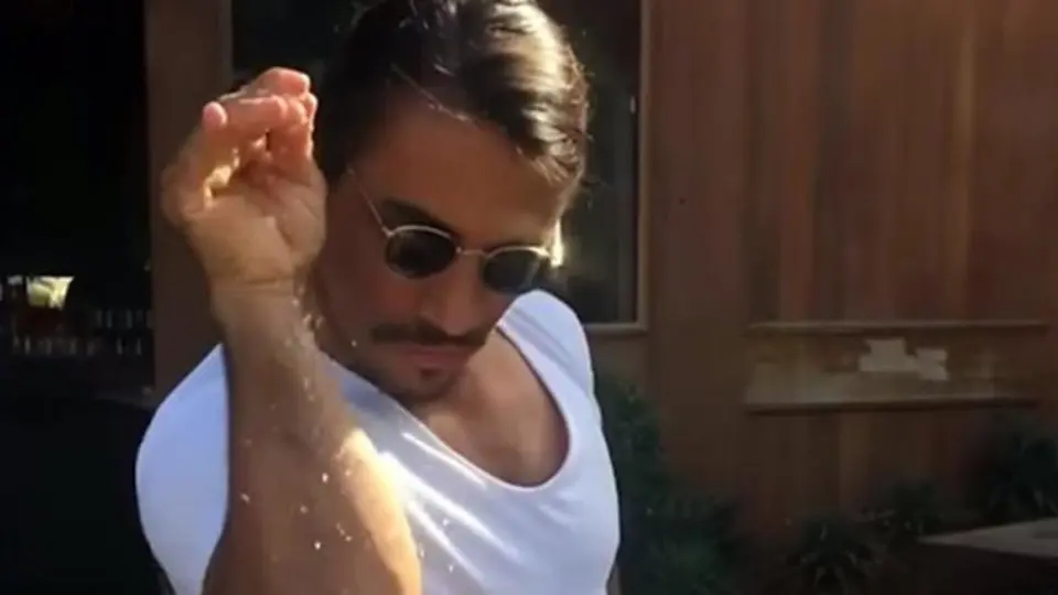 Salt Bae in sunglasses sprinkling salt down his bent forearm