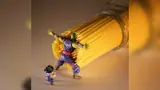 Green-skinned action figure in purple robes braces against a tipping jar of dry spaghetti, shielding a smaller figure