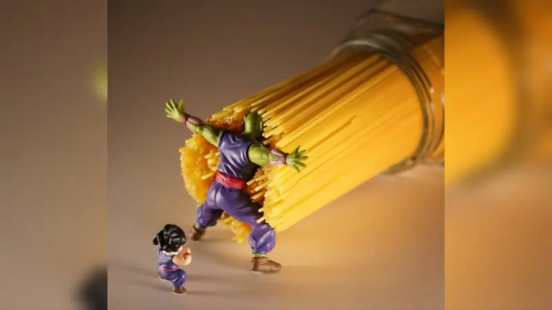 Green-skinned action figure in purple robes braces against a tipping jar of dry spaghetti, shielding a smaller figure