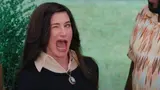 Dark-haired woman in a black top with a cream collar and cameo necklace winking with her mouth wide open outdoors