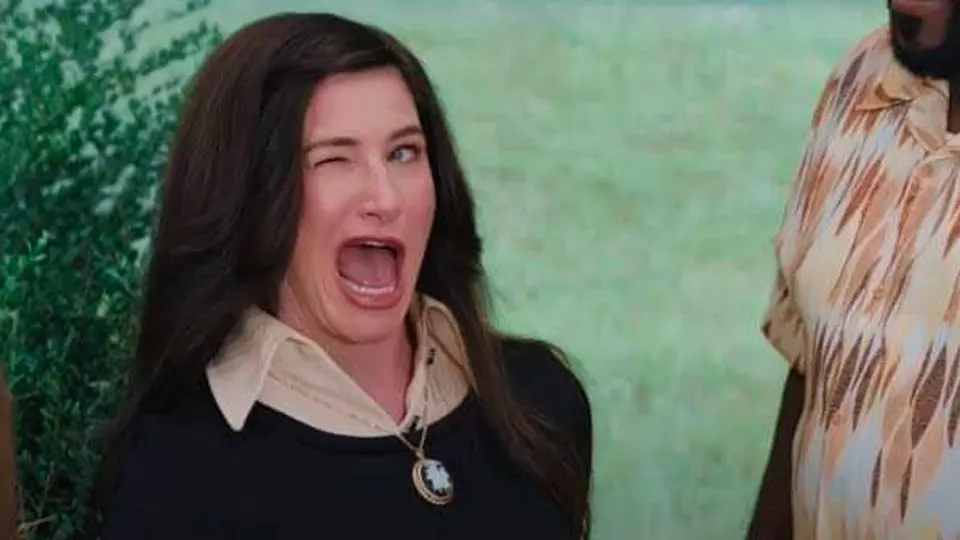Dark-haired woman in a black top with a cream collar and cameo necklace winking with her mouth wide open outdoors