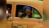 Grinning young man in a blue cap leaning out of an orange taxi window holding a camera, "RATES 25¢" sign