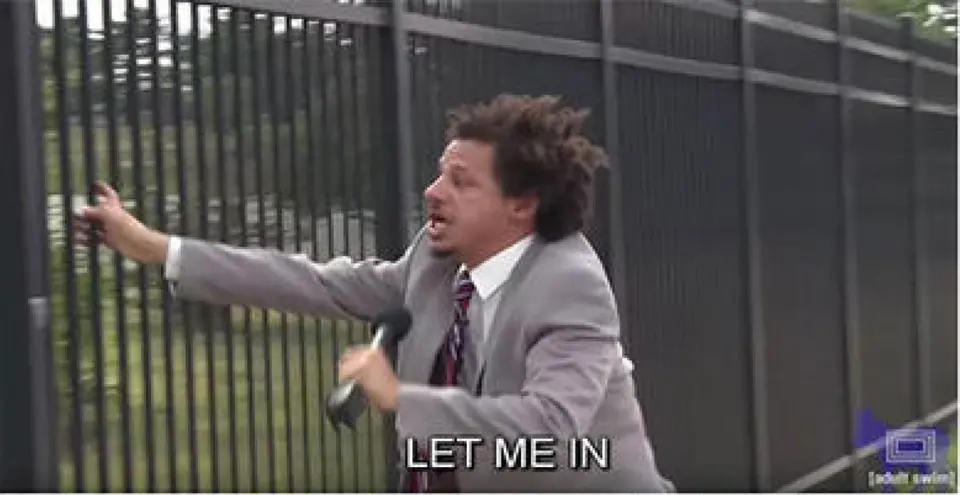 Man in a grey suit with wild hair gripping a metal fence and shouting, subtitled "LET ME IN"