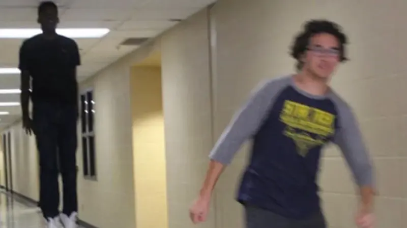 School hallway photo of one boy appearing to hover in midair while another in a raglan tee runs blurrily toward the camera
