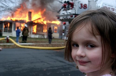A girl smirking at the camera as a house burns behind her